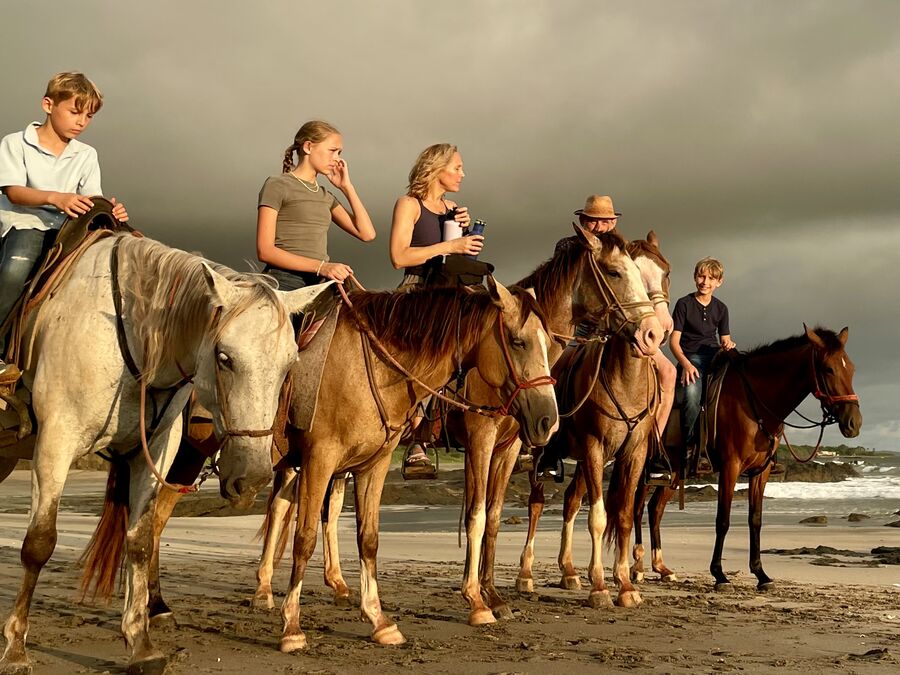 Family on horseback along the beach at Playa Junquillal at golden hour