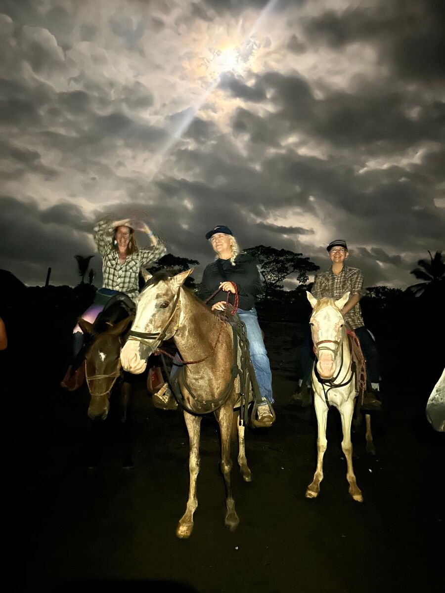 Riders on horseback under a bright moon breaking through clouds